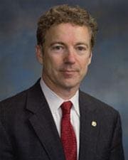 A man in suit and tie standing next to wall.